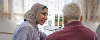 Haus St. Michael Eine junge Pflegerin mit Kopftuch füttert einen älteren Herrn.