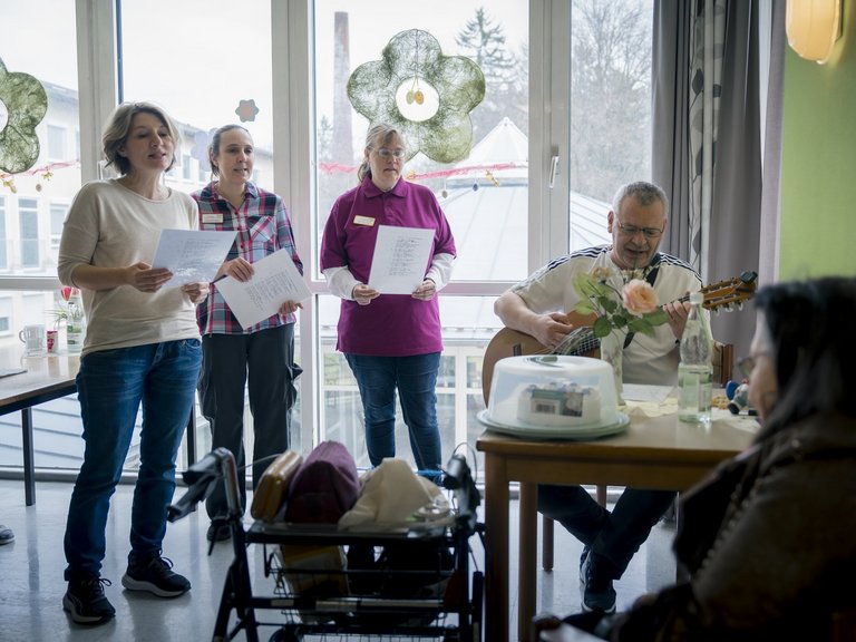 Drei Frauen singen, ein Herr spielt Gitarre und eine Frau hört zu.